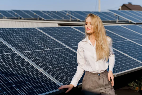 Woman leans on solar panels. Blonde dressed white formal shirt on the power plant. Free electricity for home. Green energy. Solar cells power plant business.