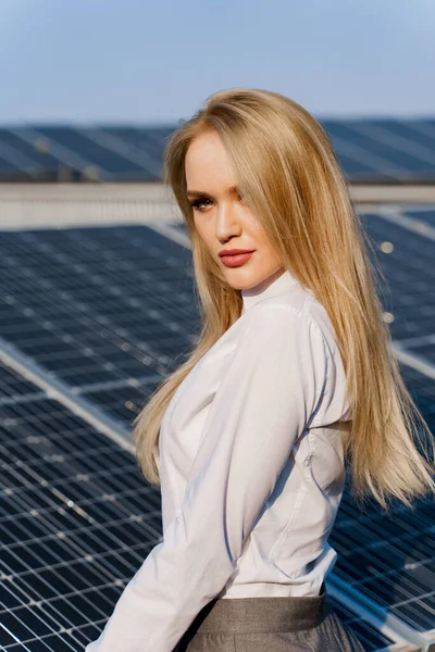 Close-up portrait of blonde model near solar panels. Woman dressed white formal shirt on the power plant. Free electricity for home. Green energy. Solar cells power plant business.