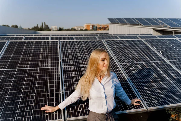 Woman leans on solar panels. Blonde dressed white formal shirt on the power plant. Free electricity for home. Green energy. Solar cells power plant business.