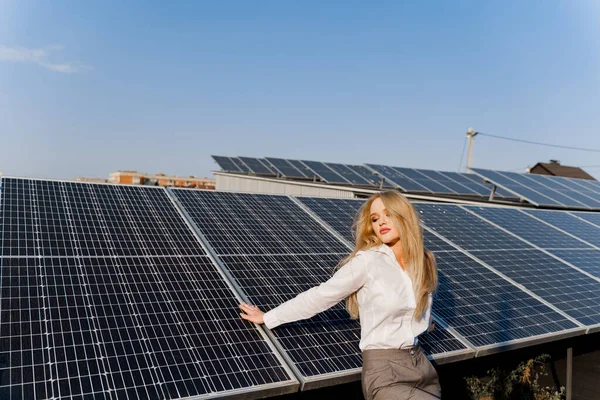 Woman leans on solar panels. Blonde dressed white formal shirt on the power plant. Free electricity for home. Green energy. Solar cells power plant business.