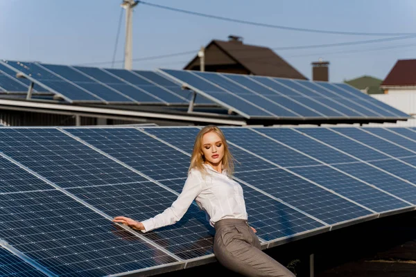 Girl and solar panels stands in row on the ground at sunset. Woman dressed white formal shirt on the power plant. Free electricity for home. Green energy. Solar cells power plant business.
