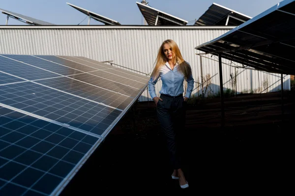 Girl walks between 2 Solar panels row on the ground at sunset. Woman investor wears formal white shirt. Free electricity for home. Sustainability of planet. Green energy.