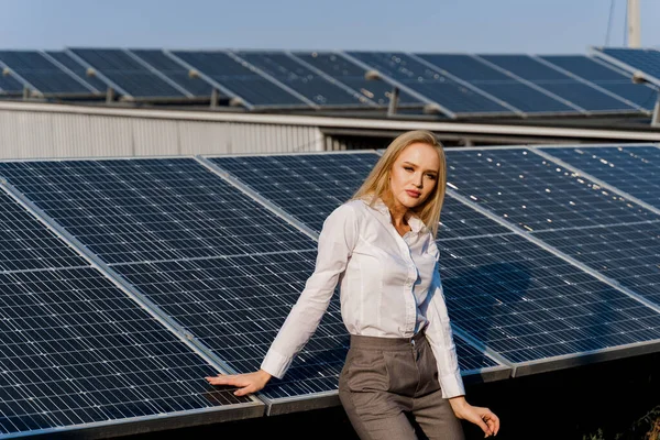Girl and solar panels stands in row on the ground at sunset. Woman dressed white formal shirt on the power plant. Free electricity for home. Green energy. Solar cells power plant business.
