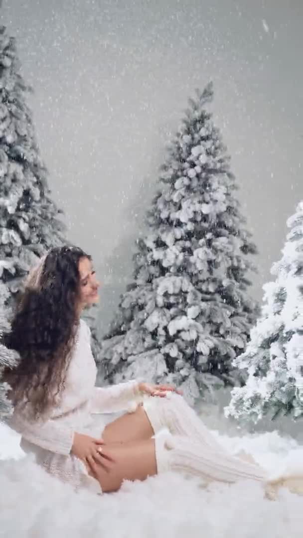 Glad flicka ler och vidrör fallande snö på kvällen nyår 4k vertikal video. Ung kvinna nära stora snöiga granar på vintern dag före jul firande — Stockvideo