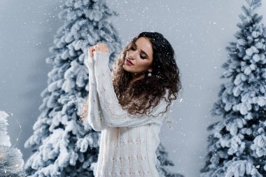 Yeni yıl kutlaması. Kar yağan mutlu kız. Sıcak beyaz kazak ve beyaz çorap giymiş genç bir kadın. Karlı bir günde kış tatili