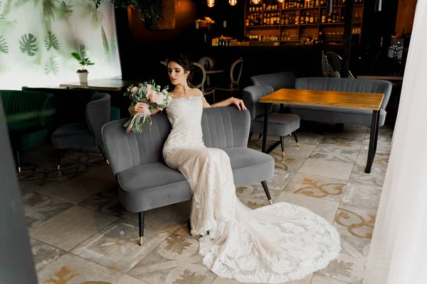 Bride in wedding dress and bridal veil seats on fashion chair in cafe. Advert for social networks for wedding agency and bridal salon
