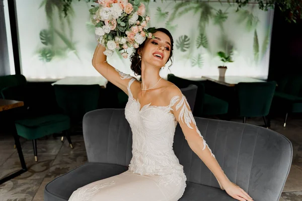 Bride in wedding dress and bridal veil seats on fashion chair in cafe. Advert for social networks for wedding agency and bridal salon