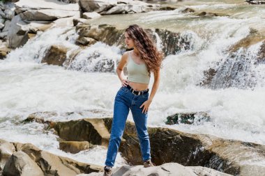 Kız Karpat dağlarında seyahat ediyor ve özgürlüğü hissediyor. Dağ nehrinde şelale. Şelale şelalesi ve güzel genç bir kadın.