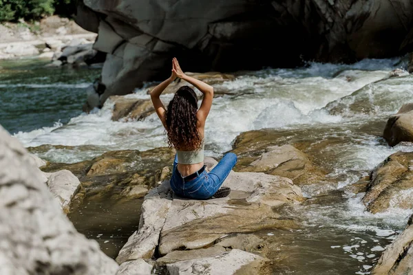 Yoga on the rocks near waterfall in mountain river. Girl is travelling in Karpathian mountains and feeling freedom. Cascade waterfall and beautiful young woman