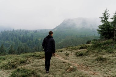 Dağın tepesine doğru yürüyüp tırmanıyor. Erkekler seyahat ediyor ve dağın dibinde dikiliyor ve zirveyi izliyor..