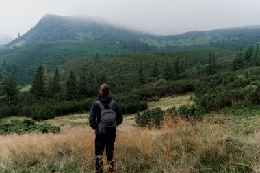 Dağın tepesine doğru yürüyüp tırmanıyor. Erkekler seyahat ediyor ve dağın dibinde dikiliyor ve zirveyi izliyor..