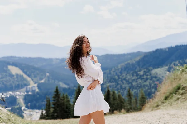 Girl traveler is smiling in the mountains. Attractive woman posing on the green hills background. Advert for travel agency. Tourism