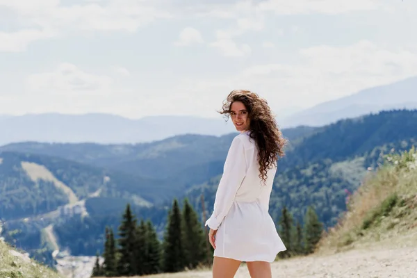 Girl traveler is smiling in the mountains. Attractive woman posing on the green hills background. Advert for travel agency. Tourism