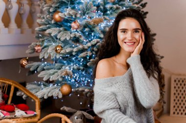 Noel ağacının yanındaki kız gülümsüyor ve poz veriyor. Yeni yıldan önce sezonluk reklamlar. Evde Noel 'i kutluyoruz.