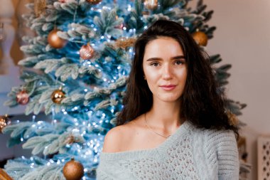 Noel ağacının yanındaki kız gülümsüyor ve poz veriyor. Yeni yıldan önce sezonluk reklamlar. Evde Noel 'i kutluyoruz.