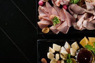 Şarküteri ve peynirli pano, farklı türde et ve peynir. Siyah tabakta tütsülenmiş et. Lezzetli parmesanlı, dorblu, yumuşak peynirli, camembert peynirli yemek tahtası..