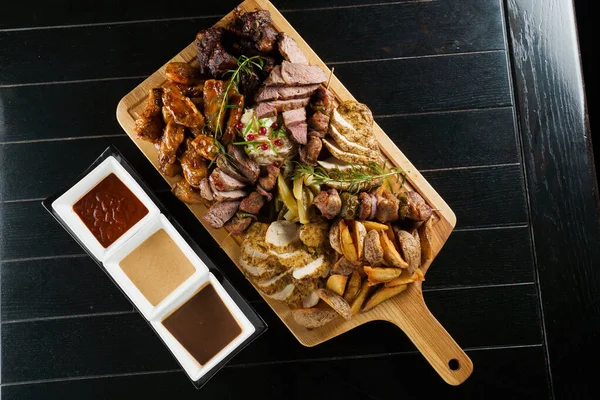 Domuz kebabı. Siyah tabakta ızgara lezzetli et. Patates, et ve sosis..