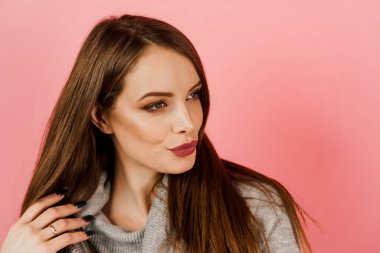 Pembe arka planda gri süveter giyen bir kadının yakın plan güzel portresi. Profesyonel model stüdyoda poz veriyor. Kafkasyalı mutlu kızın yaşam tarzı