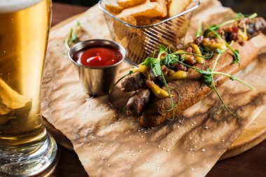 Izgara sosisli sandviç, sarı hardallı bira ve ahşap zemin üzerinde ketçap. Patates kızartması ve soslu sandviç..