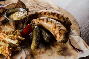 Bira ve sebzeli ızgara sosis, salatalık turşusu, lahana salatası sosu ve parşömen üzerinde ekmek..