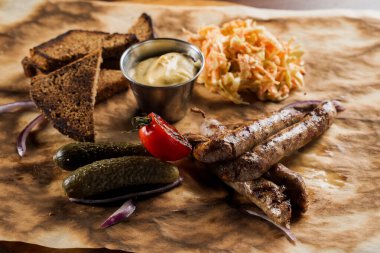 Bira ve sebzeli ızgara sosis, salatalık turşusu, lahana salatası sosu ve parşömen üzerinde ekmek..