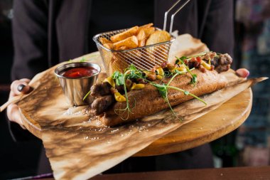 Garson siparişi ziyaretçiye götürür. Sarı hardallı ızgara sosisli sandviç ve ahşap arka planda ketçap. Patates kızartması ve soslu sandviç..