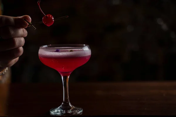 Classic Pink Lady cocktail closeup with flower and cherry on bar counter