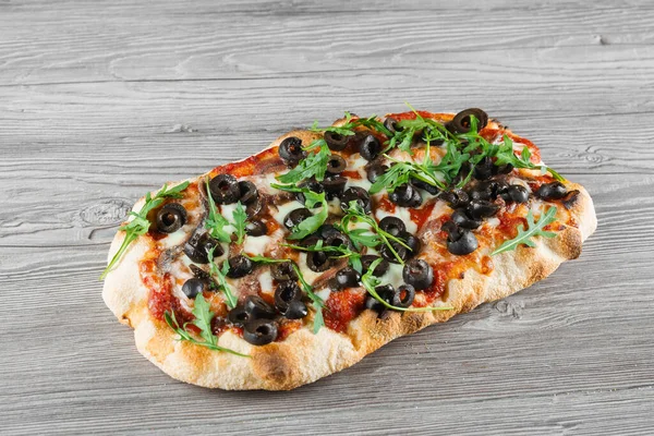 Gri ahşap arka planda Pinsa romana İtalyan mutfağı. Scrocchiarella geleneksel yemeği. Pizzacıdan yemek teslimatı. Pinsa, et, roka, zeytin, peynir..