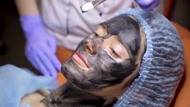 A bőrgyógyász fekete maszkot kent az arcára lézeres fotorejuvenáció és szénhámlás miatt. Bőrgyógyászat és kozmetika. Sebészeti lézerrel. — Stock videók