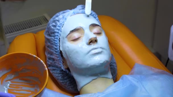 Genç bir kızın yüzü ve teni için nemlendirici maske. Yenilenme için spa prosedürü. Güzellik uzmanı maske sürüyor. Tıp kliniğinde dermatoloji — Stok video