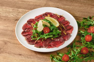 Carpaccio salata, domates ve limonlu eti ahşap bir masada beyaz bir tabakta dilimledi..