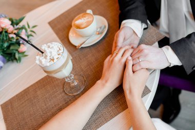 Gelin ve damat el ele tutuşuyor. Romantik bir an. Kapuçino ve marşmelovlu latte..