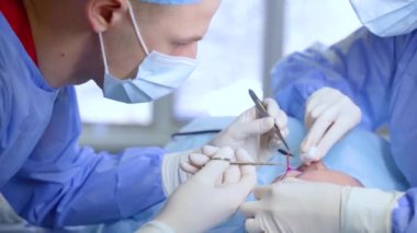 Tıbbi klinikte yüz bölgesinin değiştirilmesi için Blepharoplasty estetik ameliyatı. İki doktor kadınlar için estetik ameliyat yapıyor. Cerrah göz kapağına dikiş atar.
