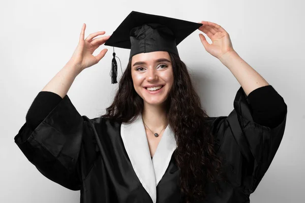 Graduate girl with master degree in black graduation gown and cap on white background. Happy young woman careerist have success in her business.