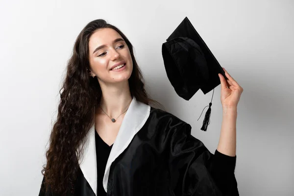 Graduate girl with master degree in black graduation gown and cap on white background. Distance learning online. Study at home. Graduation from college.
