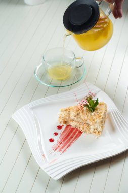 Napolyon keki, kırmızı çikolata, nane ve böğürtlen reçeli ile süslenmiş beyaz bir tabakta, çaydanlıkta portakal çayı ve şeffaf bir fincanda. Pasta ve kremalı pasta..