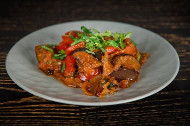Adjapsandali Gürcistan yemeği koyu ahşap bir masada gri bir tabakta otlarla süslenmiş..