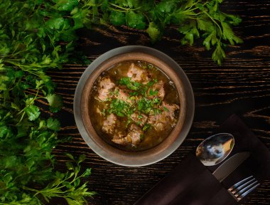 Karanlık bir tahta masada maydanoz dallarının arka planında et, at ve otlarla çorba. Güzel masa ayarları.