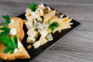 Lezzetli peynirli, cevizli peynir tabağı. Parmesan, reçel, siyah tabakta dorblu. Restorandan atıştırmalık.