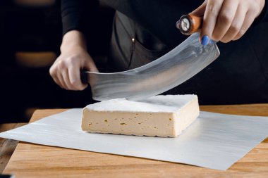 İnek sütünden krem peynir. Tahta masada peynir dilimliyorum. Organik lezzetli yemekler.