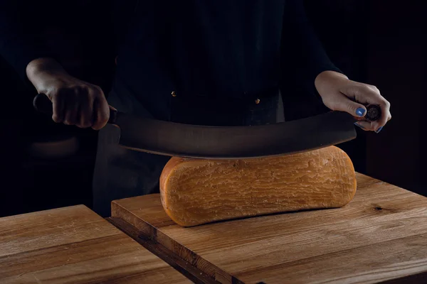 Slicing aged cheese parmesan with crystals using a cheesy dutch knife. Hard cheese with knife on dark background. Snack tasty piece of food for appetizer