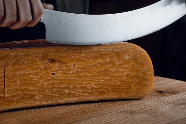 Slicing aged cheese parmesan with crystals using a cheesy dutch knife. Hard cheese with knife on dark background. Snack tasty piece of food for appetizer