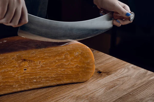 Slicing aged cheese parmesan with crystals using a cheesy dutch knife. Hard cheese with knife on dark background. Snack tasty piece of food for appetizer