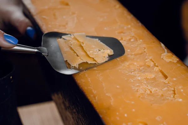 Slicing aged cheese parmesan with crystals using a slicer knife. Hard cheese with knife on dark background. Snack tasty piece of food for appetizer