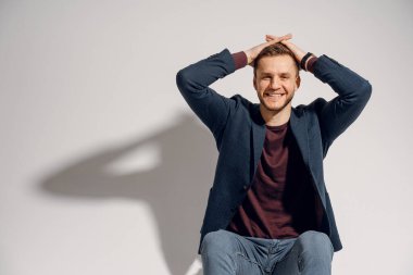 Adam gülümser ve saçlarına dokunur. Özgürlüğü hissetmek. Stüdyoda beyaz arka planda poz veren yakışıklı adam..