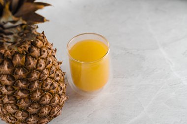 Ananas ve meyve suyu beyaz taş arka planda çift cam bardakta. Tropikal meyve kadehe sarı tropikal meyve suyu döküyor..
