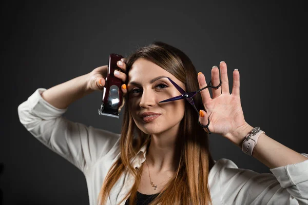 Woman barber with scissors and hair clipper in barbershop. Portrait of hairdresser for advert