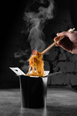 Tava kutusunda siyah arka planda pilav eriştesi buharı. Fast food teslimat servisi. Çin sokak yemeği siparişi. Siyah yemek kabında Udon