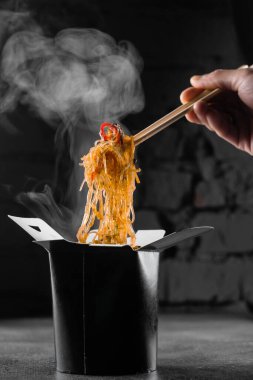 Tava kutusunda siyah arka planda pilav eriştesi buharı. Fast food teslimat servisi. Çin sokak yemeği siparişi. Siyah yemek kabında Udon