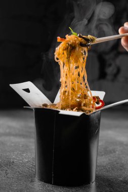 Tava kutusunda siyah arka planda pilav eriştesi buharı. Fast food teslimat servisi. Çin sokak yemeği siparişi. Siyah yemek kabında Udon